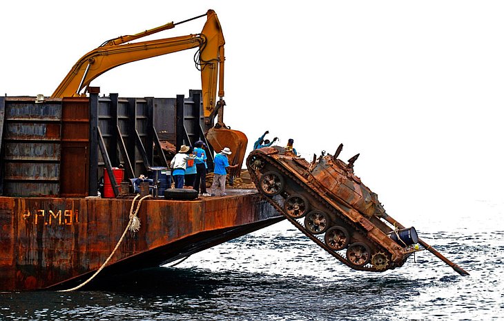 Рабочие сталкивают старый танк с корабля в море