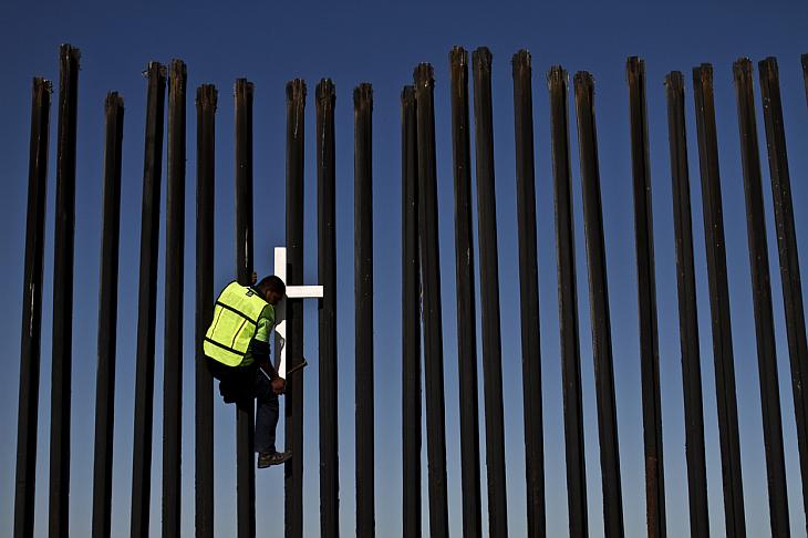 Депортированные мигранты перелезают через забор на американо-мексиканской границе в ходе подготовки к 6 ежегодному маршу мигрантов в Тихуане