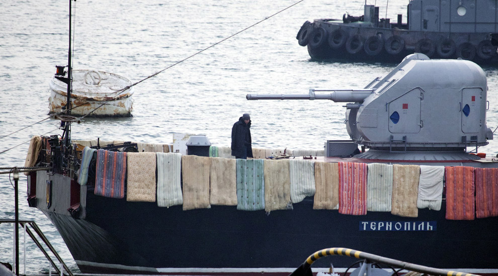 Украинский моряк наблюдает за российскими солдатами, пытающимися захватить судно „Тернополь“ в Севастополе, 4 марта 2014. Украинцы кладут одеяла и матрасы на борт кораблей, чтобы воспрепятствовать любой попытке нападения