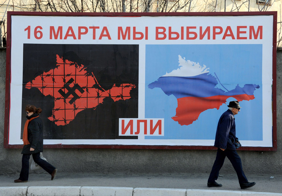 Плакат на улице Севастополя перед референдум в эти выходные, изображающий Крым со свастикой и покрытый колючей проволокой, и Крым с цветами российского флага