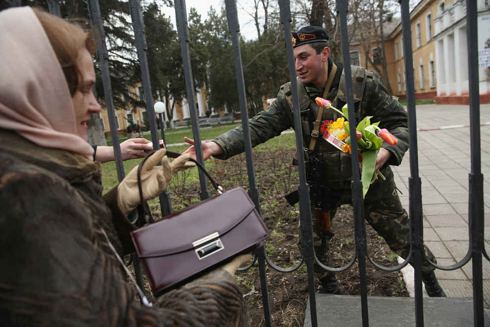 Украинский солдат принимает через забор блокированной украинской военной базы сигареты, шоколад и цветы