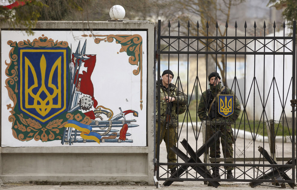 Украинские офицеры стоят за воротами воинской части в поселке Перевальное, 11 марта 2014. Пророссийские войска открыли огонь и захватили украинского военную базу в Крыму