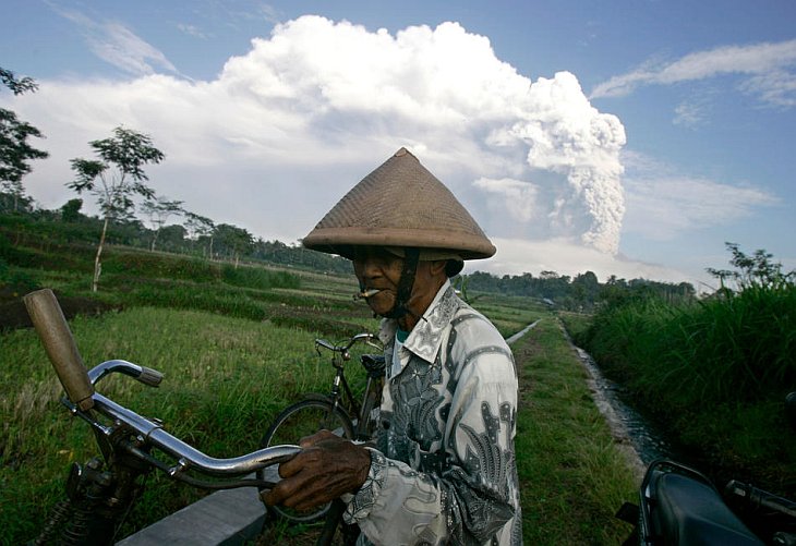 Фермер стоит на рисовом поле на фоне извергающегося вулкана Мерапи