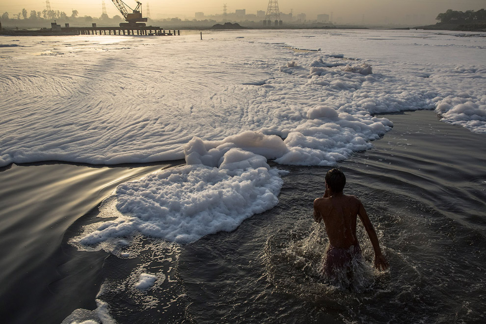 Человек купается в реке Ямуна на окраине Нью-Дели, загрязненной промышленными отходами
