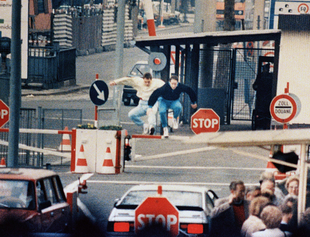 Двое жителей Восточного Берлина прыжками пытаются преодолеть пограничные барьеры