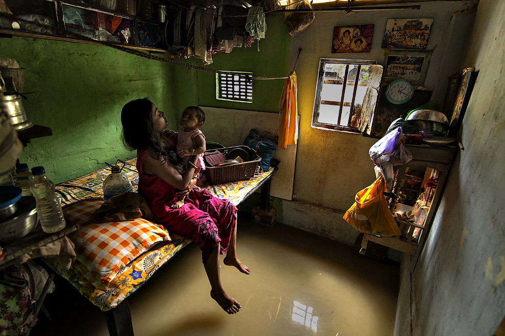 Мать играет с ребенком в затопленном помещении вблизи берегов реки Ганг, Калькутта, Индия