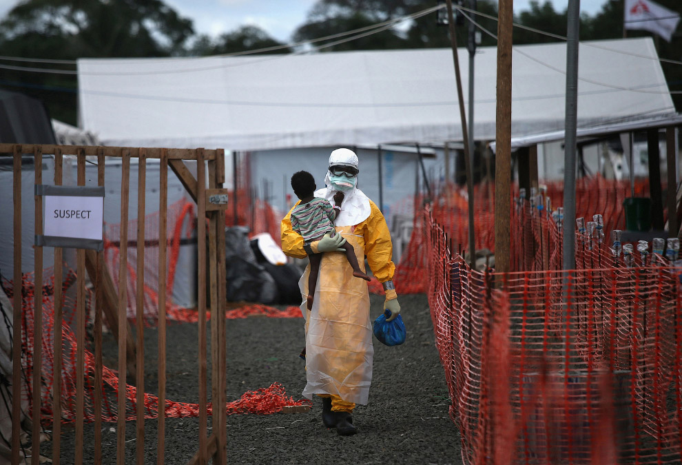 Медработник в защитной одежде несет ребенка с подозрением на вирус Эбола, Либерия
