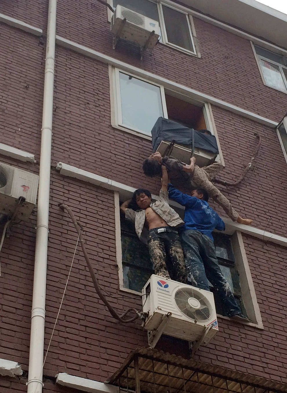 Двое поддерживают женщину в ожидании спасателей, которая выпала из окна своей квартиры, по застряла в крепеже кондиционера